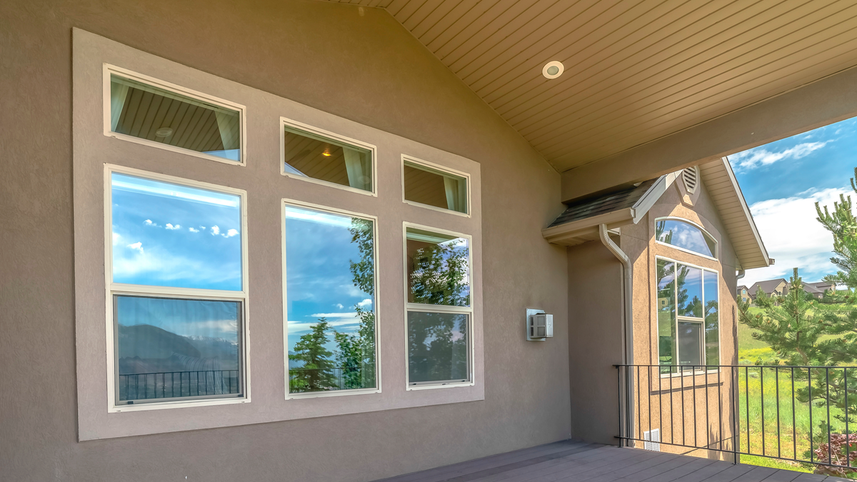 A bank of large Andersen replacement windows reflecting the sky on a modern tan stucco house in Lansing, Michigan.