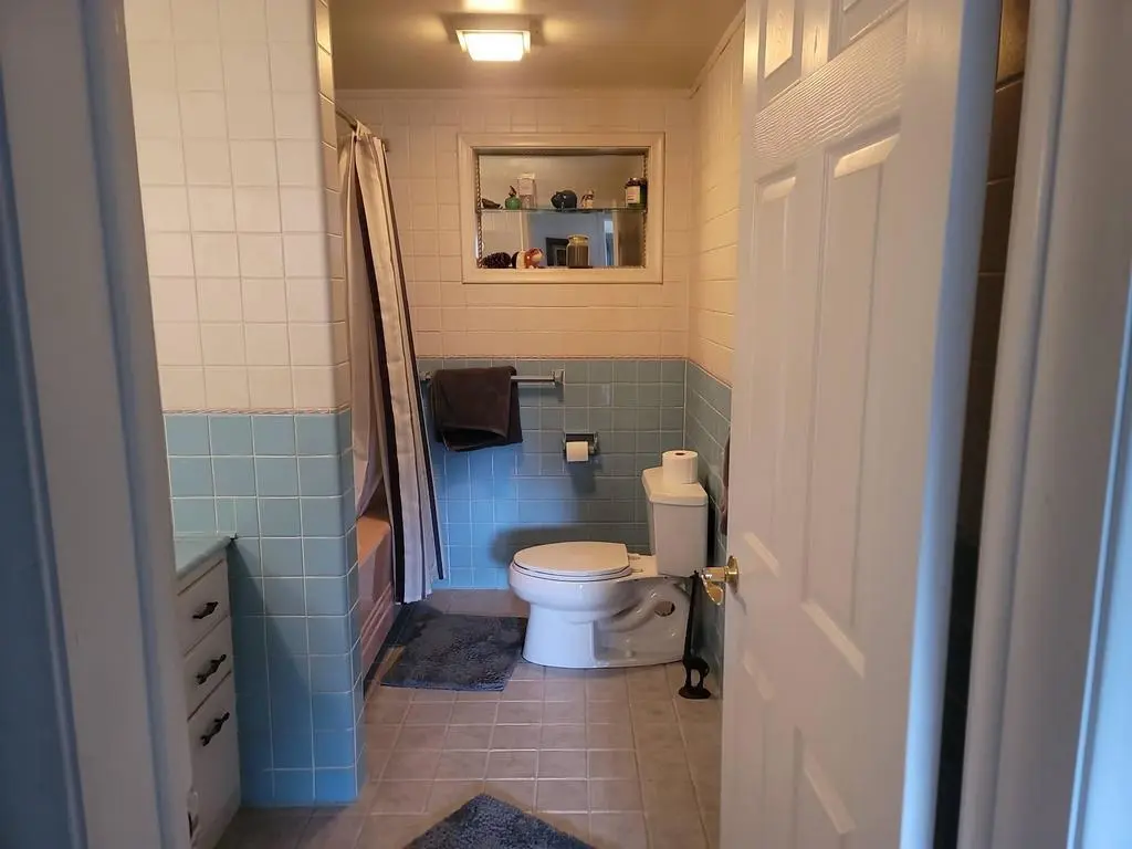 Old blue tiled bathroom wall and toilet before renovation