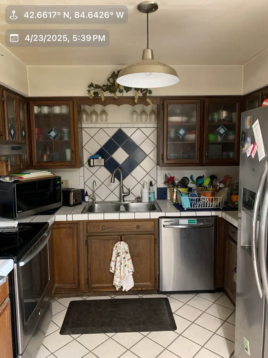 Before view of a cramped kitchen in Dimondale, MI, featuring dated wood cabinets and a tile backsplash, prior to a modern open-plan renovation.