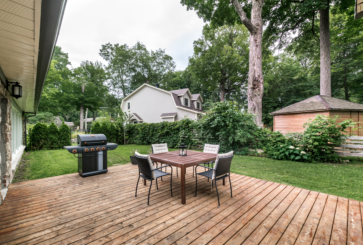 A natural wood deck in a backyard in Ada Township, Michigan, with a patio dining set and a grill overlooking the lawn.