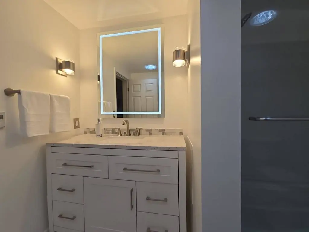 Modern white soft-close vanity with granite countertop and LED mirror in Okemos MI - After Remodel