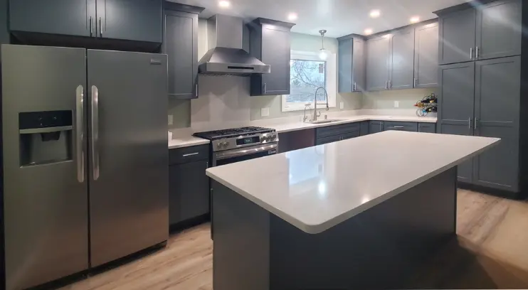 Modern kitchen renovation in Dimondale, MI, featuring dark grey shaker cabinets, a large white quartz island, stainless steel appliances, and wood-look vinyl plank flooring.