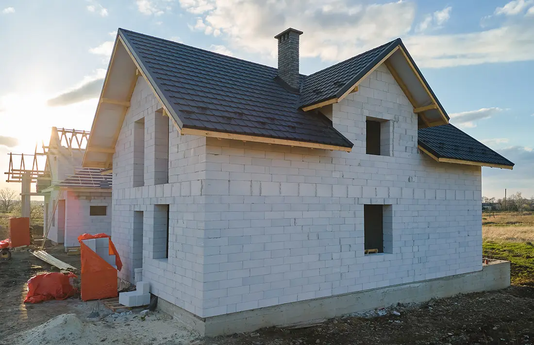 A new home construction site in Lansing, Michigan, showing a house being built with white foam block walls and a newly installed dark shingle roof. Learn how long does it take to build a new home in Michigan.