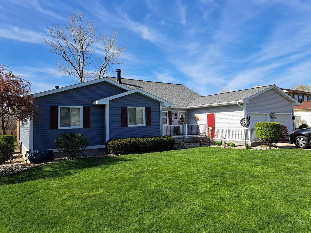 House in Holt, MI, during a CertainTeed vinyl siding remodel, with new Pacific blue siding being installed next to the existing faded light grey siding, showing a clear transition and updated house exterior.