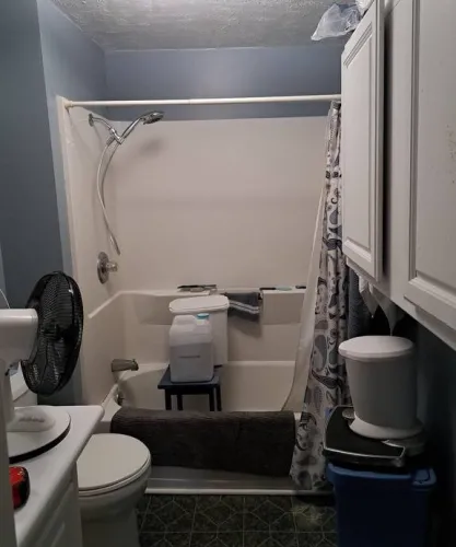 Before a custom small bathroom remodel in Mason, MI, featuring an outdated shower, blue walls, and original flooring, awaiting renovation.