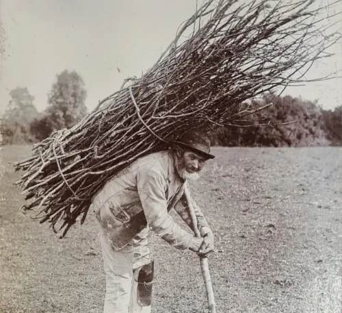 Black and white photograph of an old roof thatcher carrying a large bundle of sticks, famously featured on the Led Zeppelin IV album cover.