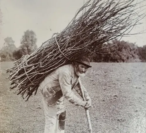 Black and white photograph of an old roof thatcher carrying a large bundle of sticks, famously featured on the Led Zeppelin IV album cover.
