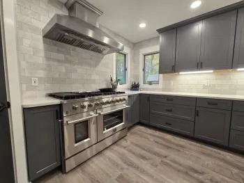 A beautiful shot of the completed custom kitchen remodel in Brighton. The design balances the deep gray of the cabinets with the brightness of the white granite countertops and backsplash. Recessed and under-cabinet lighting ensures the space is always warm and inviting, highlighting the expert craftsmanship and stunning new materials.