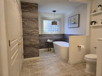 The stunning result of our custom bathroom remodel in Traverse City. The new, open-concept layout features a spacious walk-in shower, a freestanding soaking tub, and a beautiful granite-topped vanity. The heated ceramic tile floor adds a final touch of luxury.